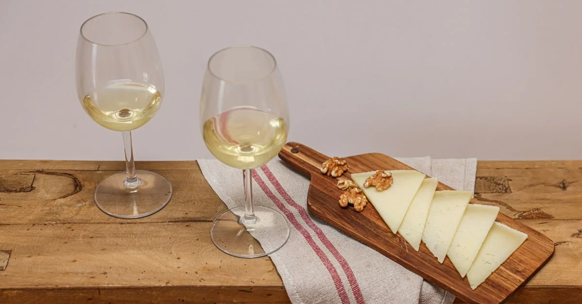 Naturaleza muerta sofisticada de vino blanco y queso en rodajas con nueces sobre una tabla de madera.