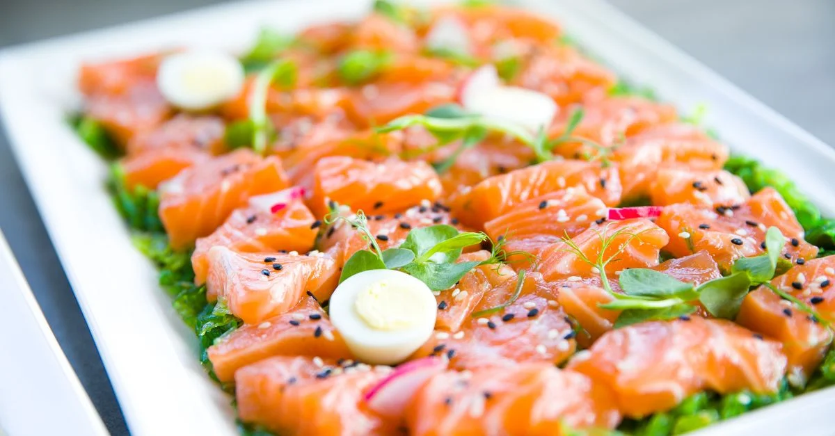 Delicioso sashimi de salmón adornado con huevos de codorniz y verduras frescas en una bandeja.