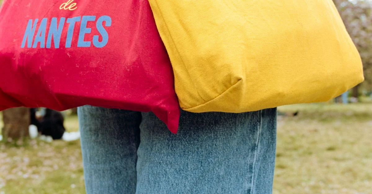 Bolsas tote vibrantes con texto de Nantes en un entorno de parque durante la primavera.