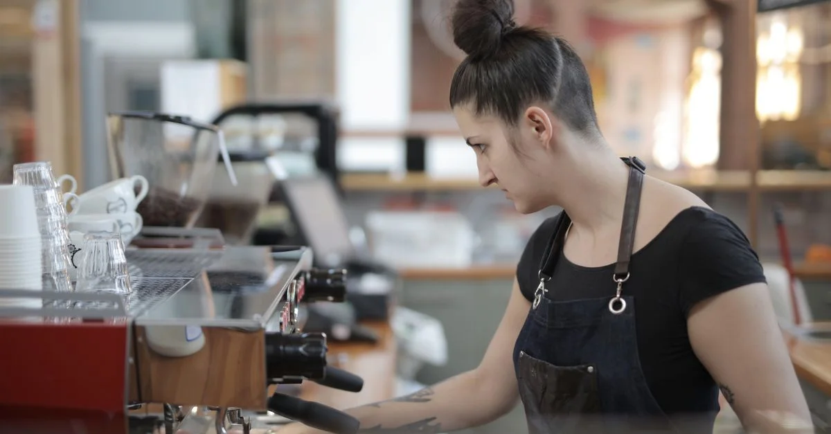 Una barista elabora café con destreza en una cafetería moderna, utilizando una máquina de espresso.