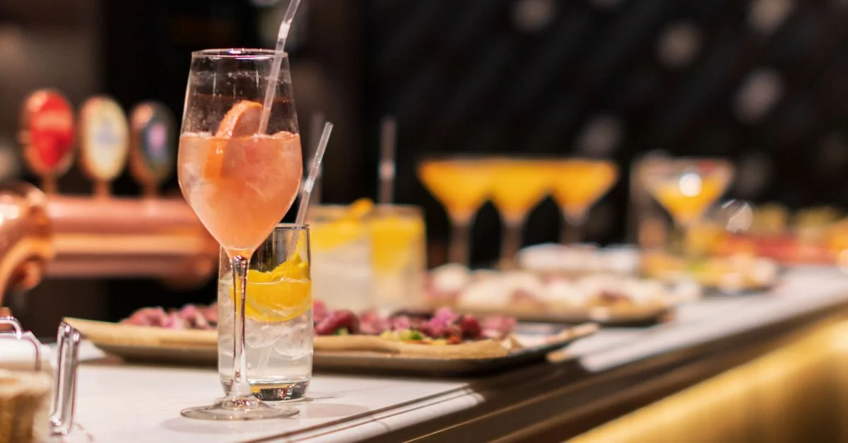 Cócteles vibrantes y aperitivos dispuestos elegantemente en una barra en un entorno elegante.