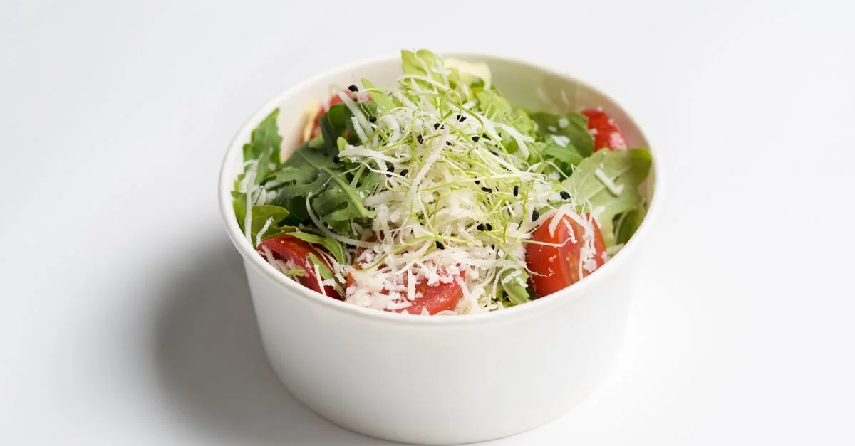 Deliciosa ensalada de la huerta con tomates cherry, hojas verdes y queso rallado en un bol.
