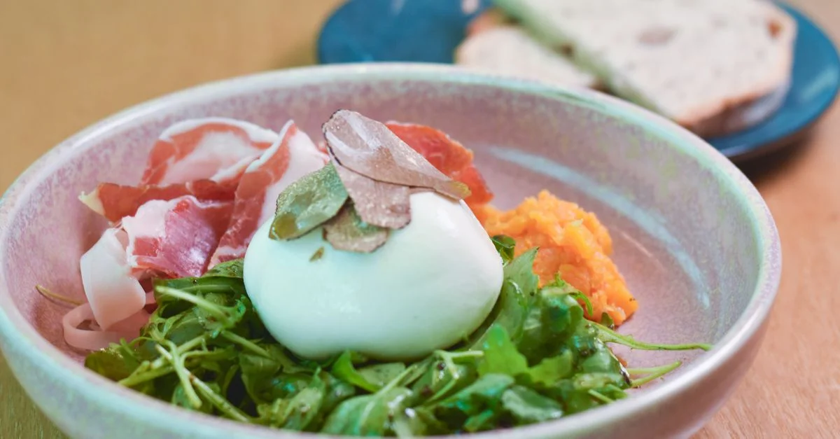 Deliciosa ensalada gourmet de burrata con jamón, rúcula y láminas de trufa servida en un bol de cerámica.