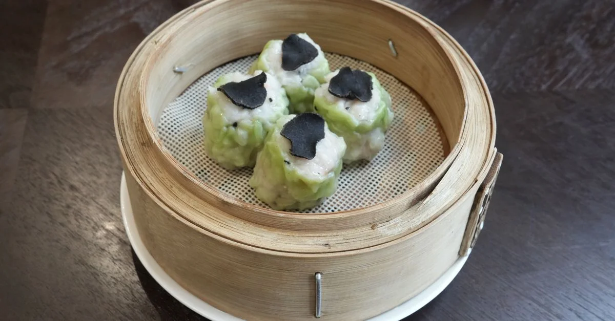 Délicieux raviolis vapeur aux tranches de truffe, servis dans un panier en bambou.