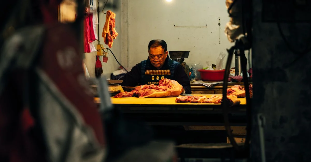 Un boucher dévoué découpe de la viande dans un cadre intérieur faiblement éclairé, concentré sur son travail.