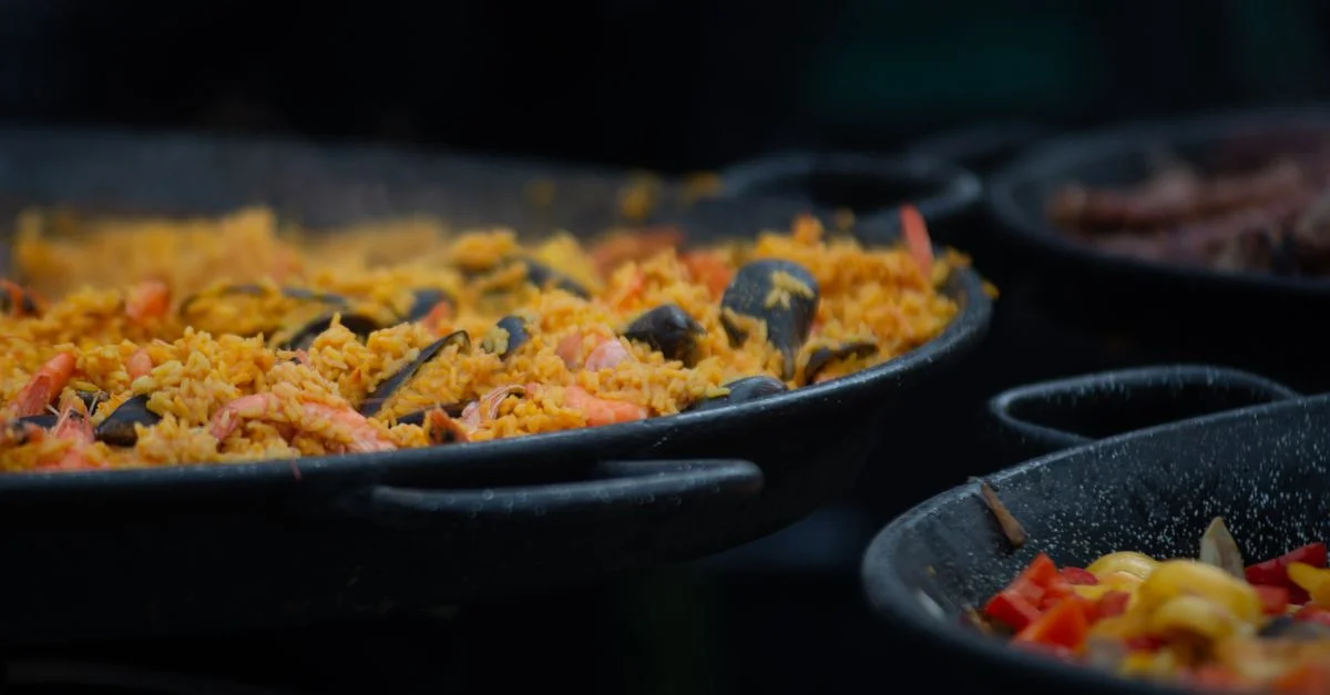 Close-up apetitoso de paella de mariscos tradicional cocinándose en una gran sartén al aire libre.