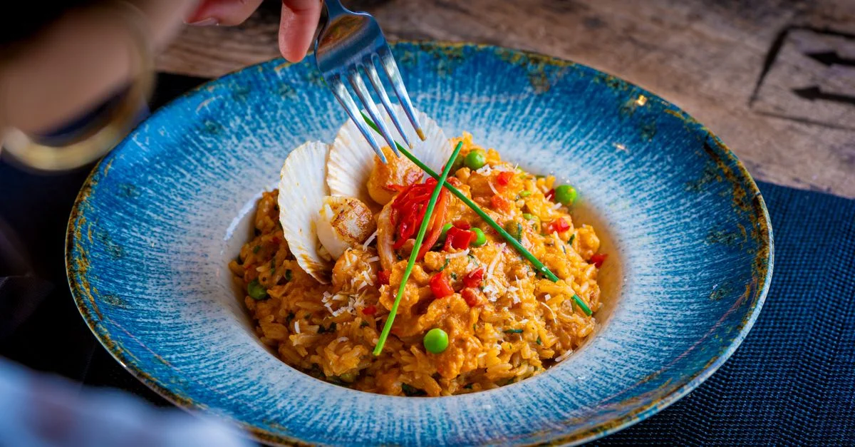 Primer plano de paella de mariscos con verduras en un cuenco de cerámica azul siendo servida.