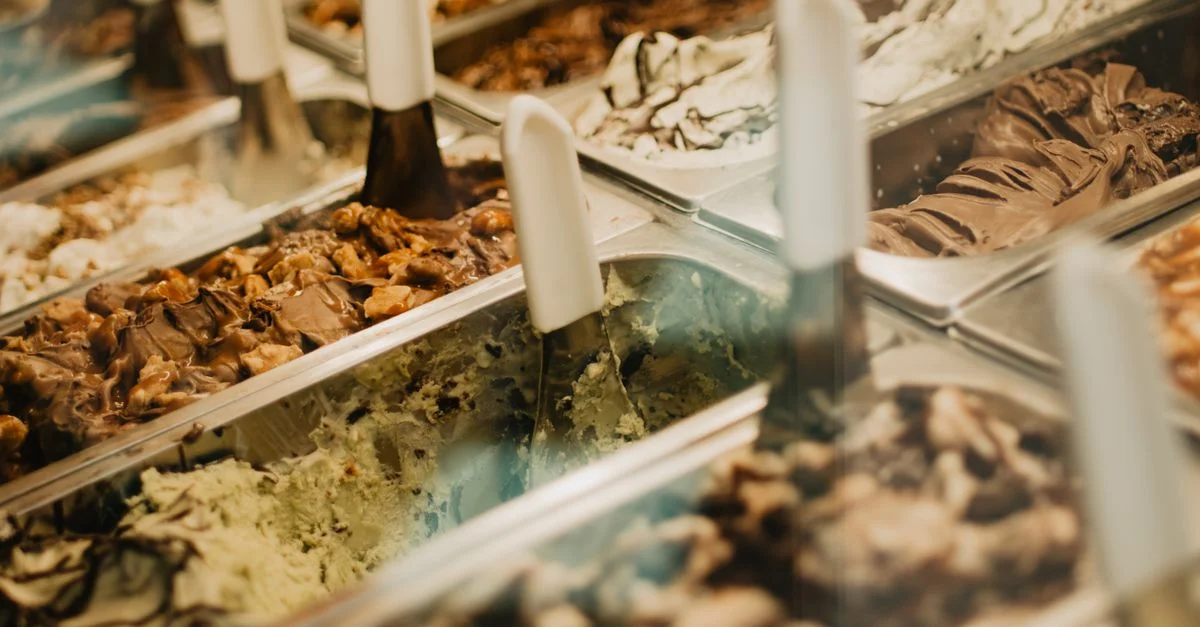 Une vitrine vivante de saveurs de gelato variées dans des plateaux, mettant en avant des textures et des couleurs riches dans une boutique de desserts.