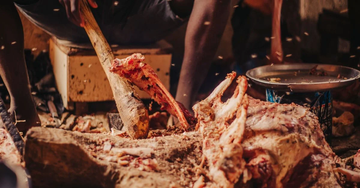 Un hombre deshuesando carne hábilmente con herramientas tradicionales en un entorno interior.