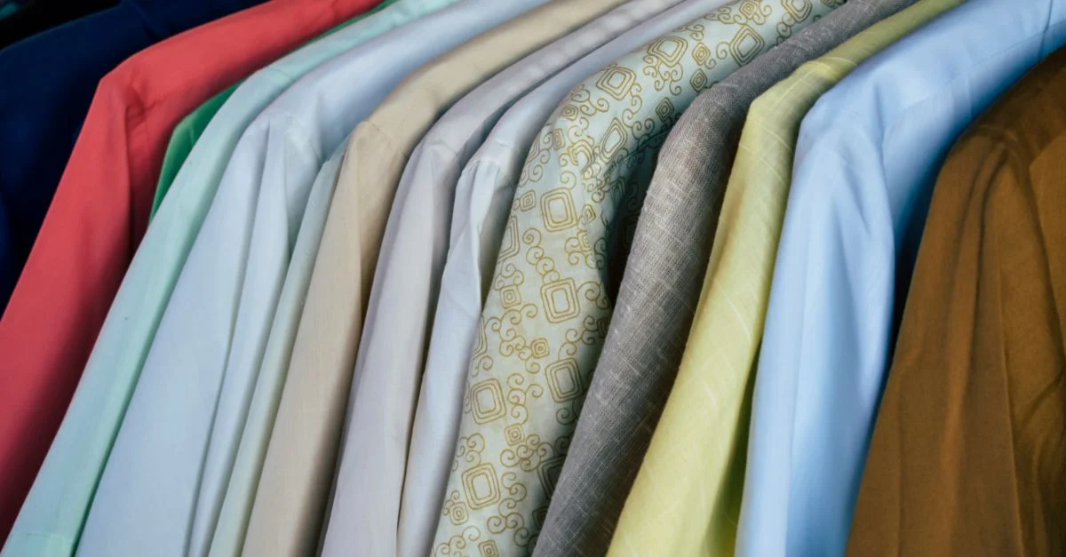 Una variedad de camisas coloridas colgadas ordenadamente en perchas de madera, mostrando diferentes tejidos.