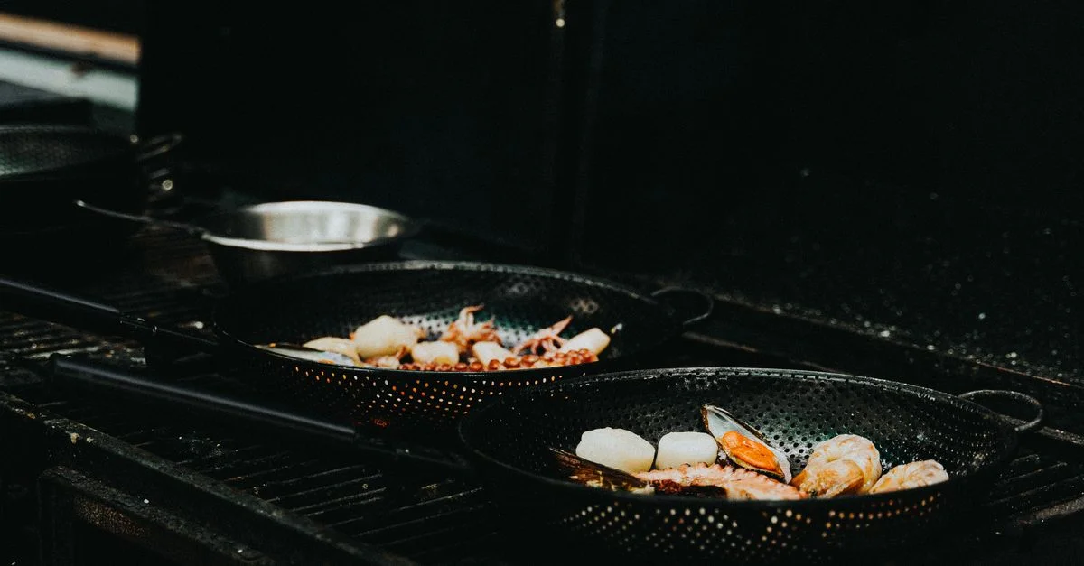 Primer plano de mariscos chisporroteando, incluyendo mejillones y vieiras en sartenes de hierro fundido en una parrilla, perfecto para entusiastas de la fotografía de alimentos.