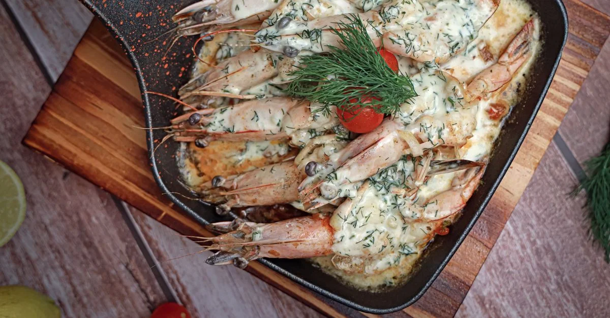 Camarones salteados en salsa cremosa con eneldo y tomates cherry en una sartén de hierro.