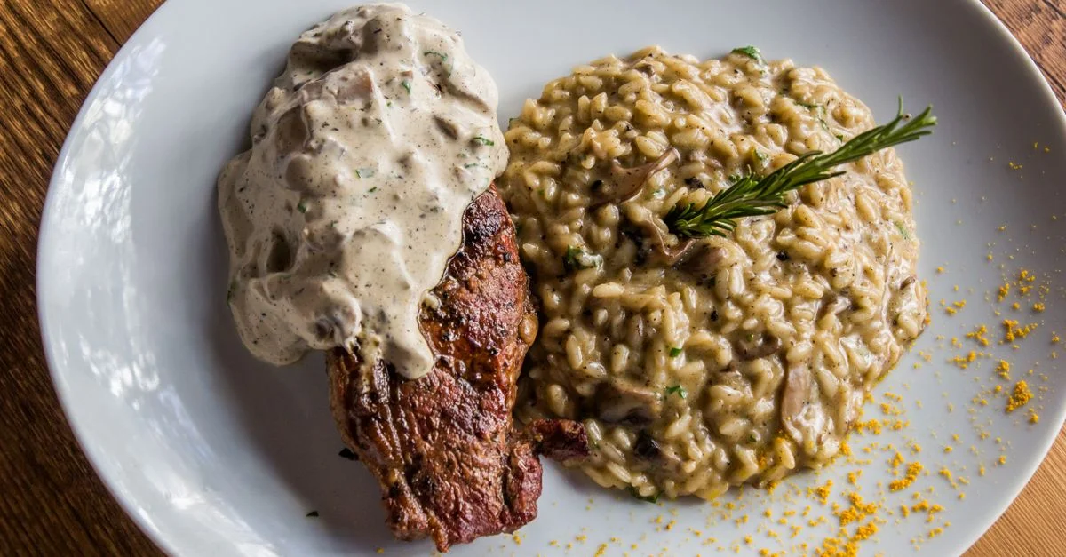 Delicioso filete cubierto con salsa servido con risotto cremoso de champiñones. Cocina italiana en un plato blanco.