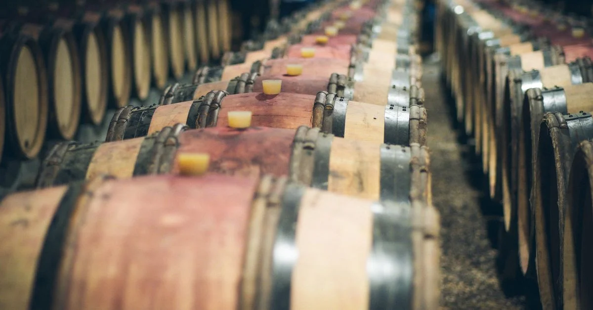 Vista en primer plano de barricas de vino de madera alineadas envejeciendo en una bodega con poca luz.