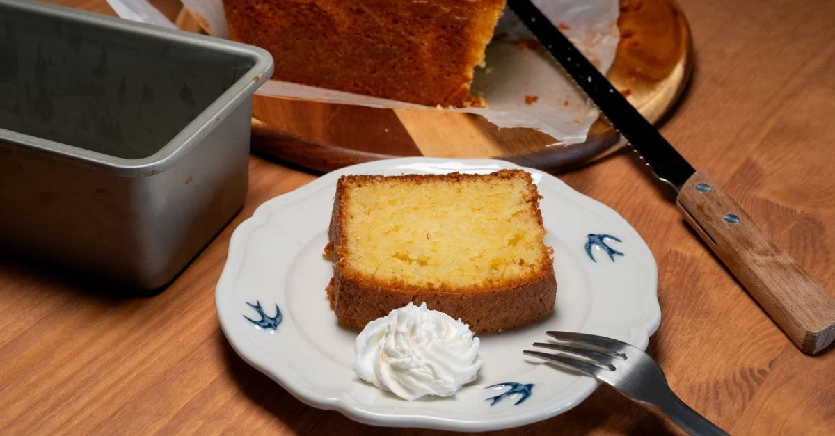 Una rebanada de bizcocho casero con una cucharada de crema batida, servida en un plato decorativo.