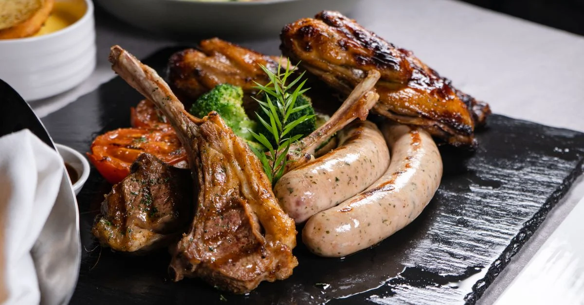 Delicioso plato de carne a la parrilla con cordero, salchichas y verduras en un plato de pizarra.