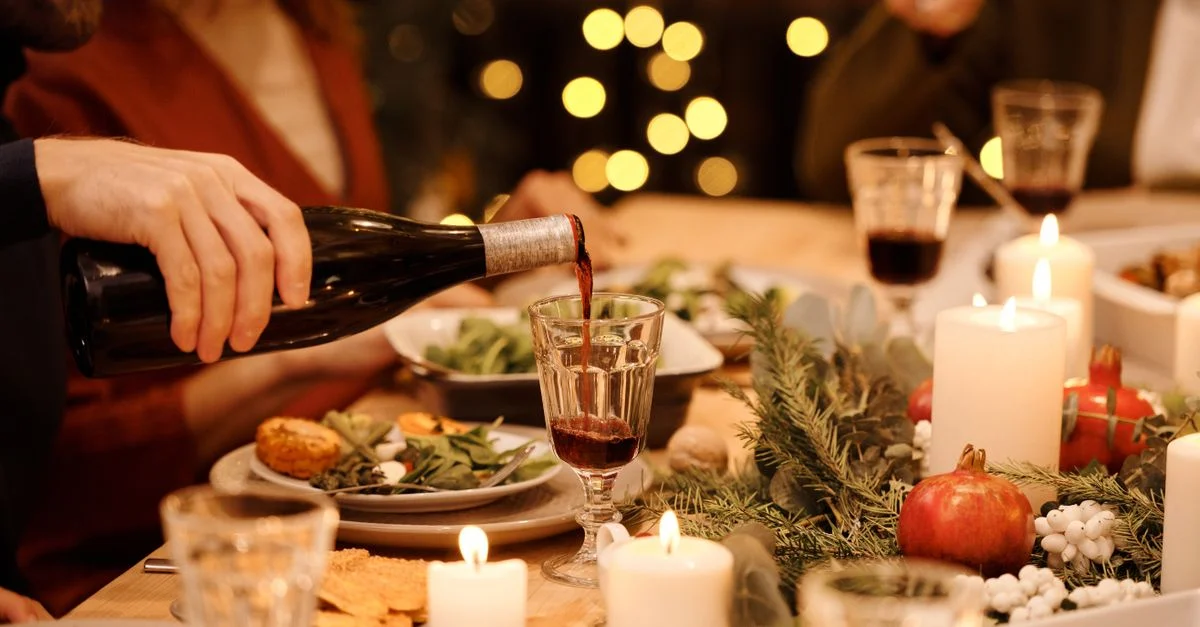 Configuración de cena festiva con decoraciones, velas y vino sirviéndose para una celebración alegre.