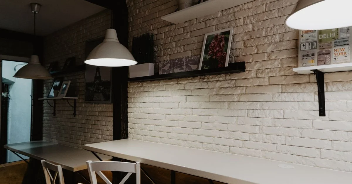 Interior acogedor de café con diseño moderno, lámparas colgantes y estanterías decorativas en una pared de ladrillo.