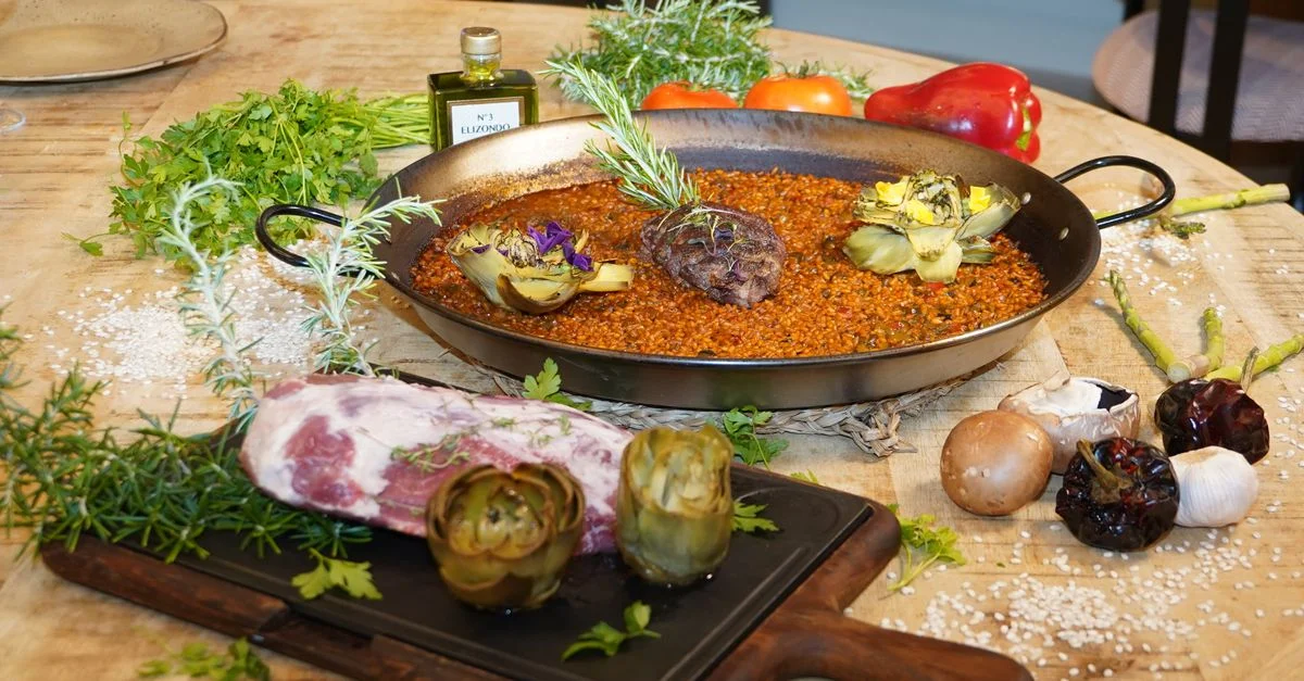 Deliciosa paella española con alcachofas y carnes selectas sobre una mesa rústica.