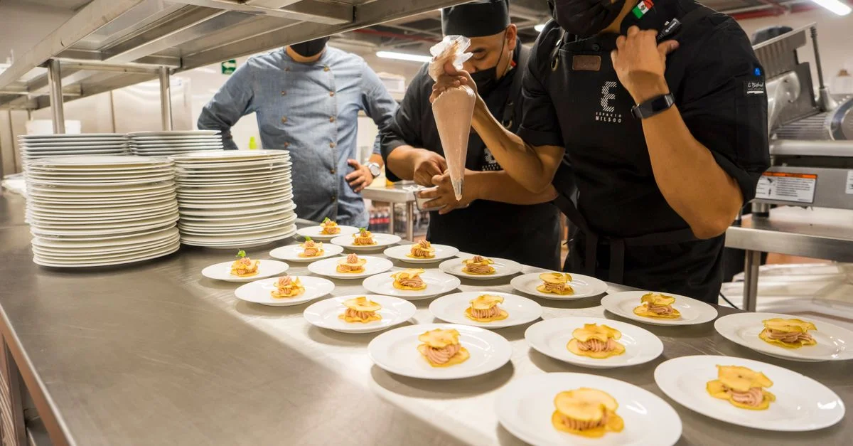 Equipo de chefs presentando creativamente aperitivos gourmet en una cocina comercial.