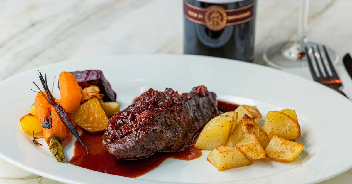 Deliciosa carne gourmet servida con verduras asadas y vino tinto.