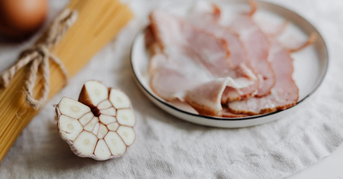 Una disposición visualmente atractiva de bacon, ajo, huevos y pasta sobre un fondo de lino.