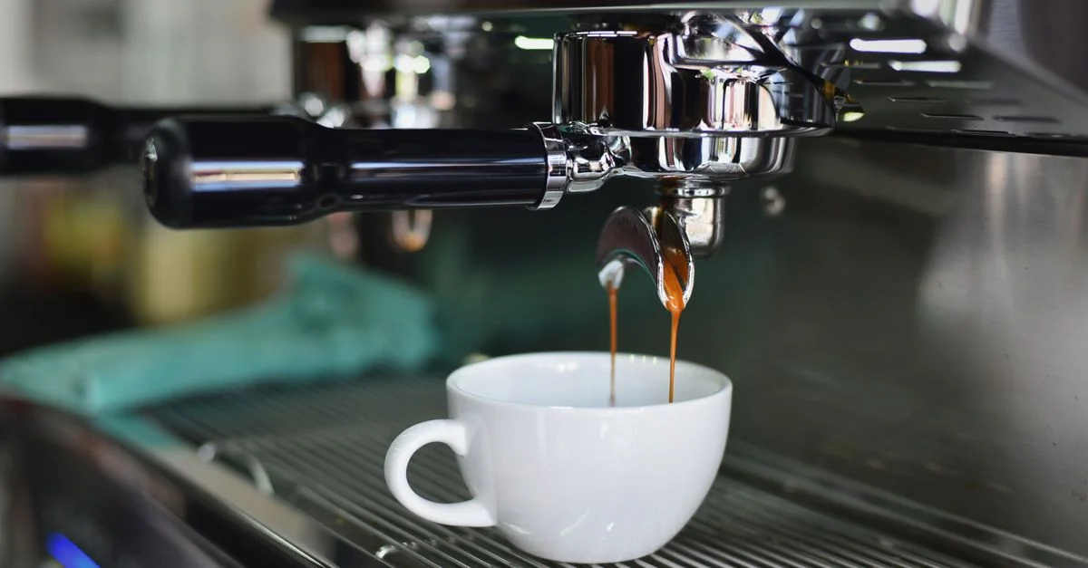 Primer plano de espresso vertiéndose de una brillante máquina de café en una taza blanca, perfecto para amantes de la cafeína y el arte barista.