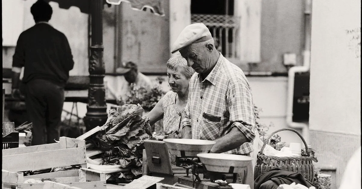 Photo en noir et blanc d'un couple âgé travaillant dans un marché de rue en milieu urbain.