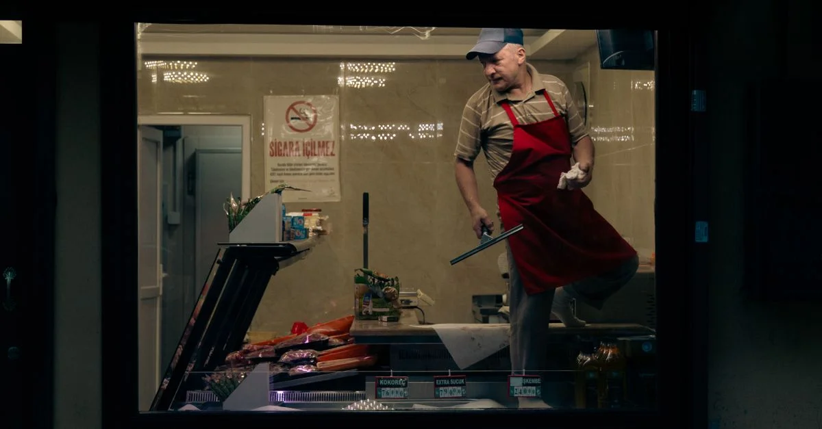 Un carnicero dentro de una tienda en Bursa, Turquía, con delantal y gorra, trabajando con carne.
