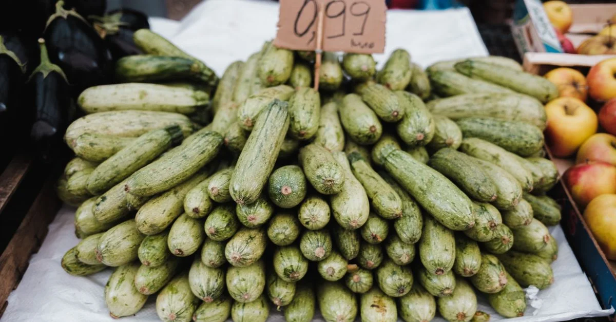 Pila de calabacines frescos en exhibición con precio en un mercado de agricultores local.