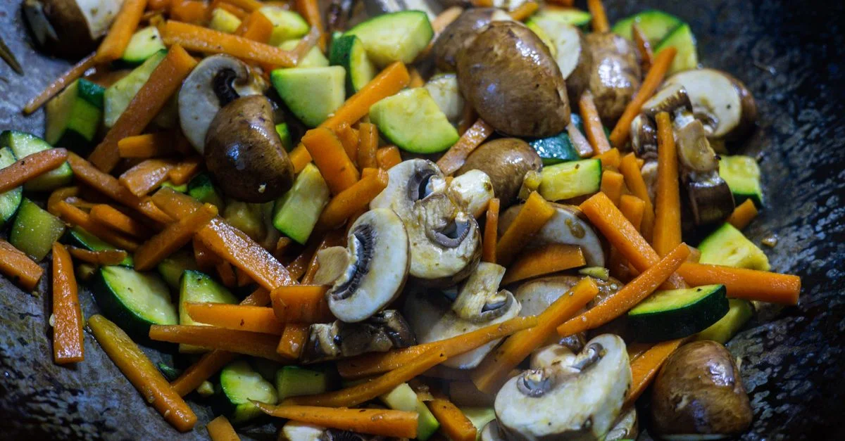 Primer plano de verduras vibrantes salteadas, incluyendo champiñones, zanahorias y calabacines en un wok.