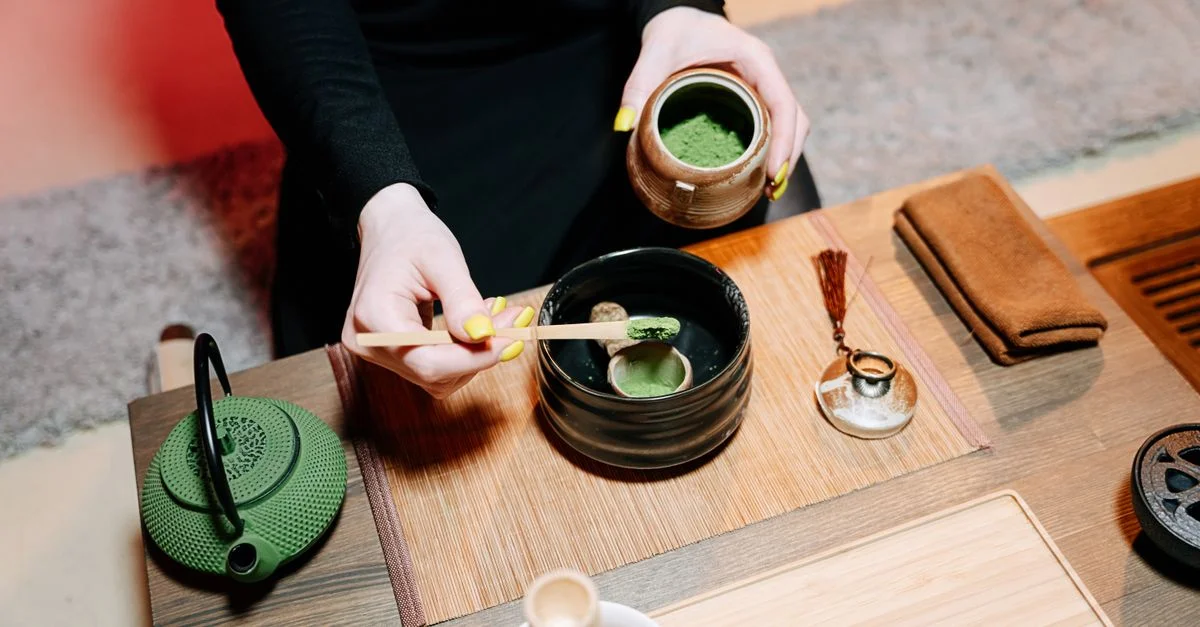 Manos preparando té matcha en una ceremonia japonesa tradicional con tonos verdes vibrantes y terrosos.