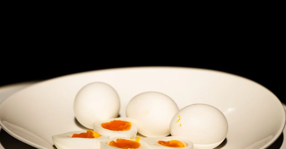 Une assiette blanche d'œufs durs, certains tranchés, sur fond sombre.