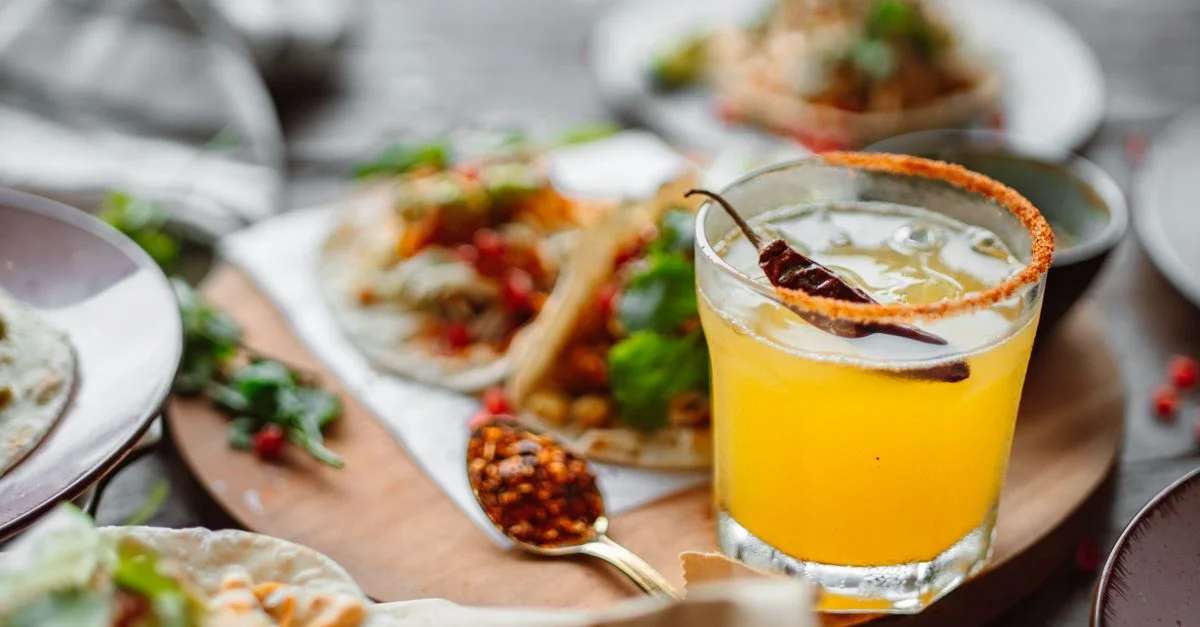 Primer plano de tacos mexicanos y un cóctel de margarita picante sobre una mesa de madera.