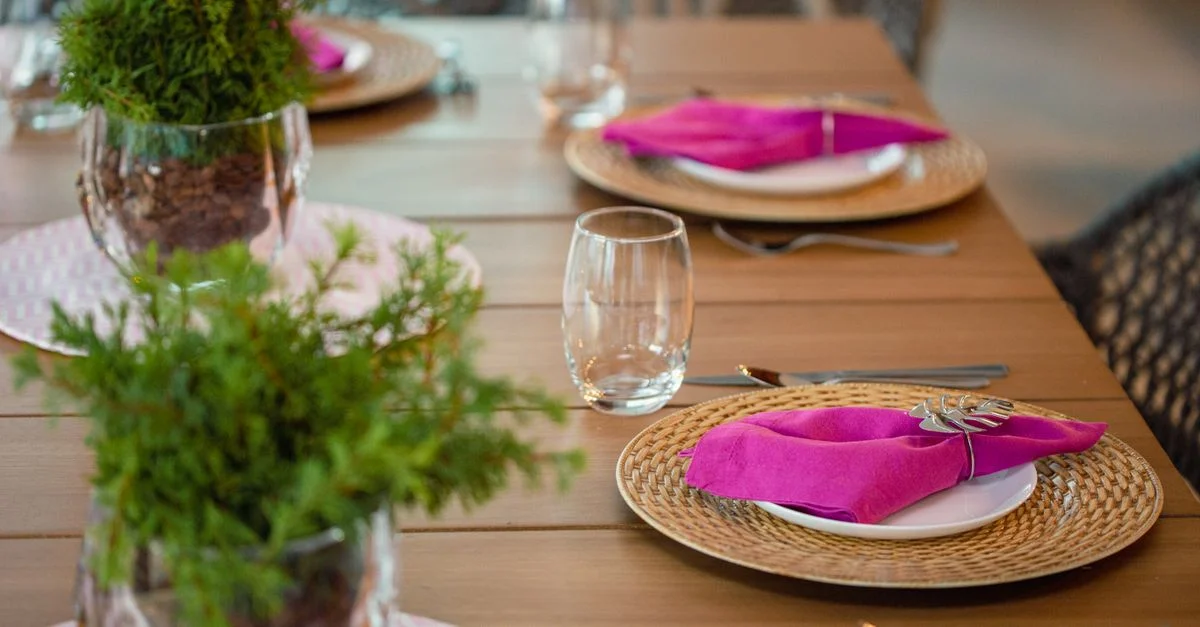 Una mesa de comedor bellamente dispuesta con servilletas rosas y centros de mesa de plantas, perfecta para un evento con estilo.