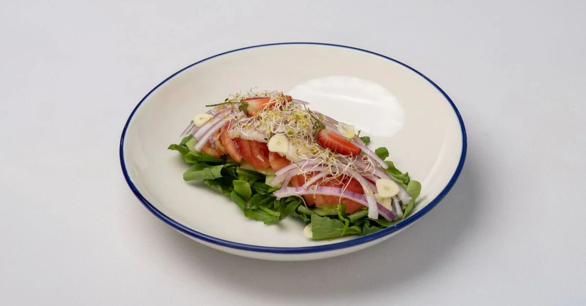 Deliciosa ensalada fresca con tomates, brotes, cebollas y ajo sobre un fondo blanco.