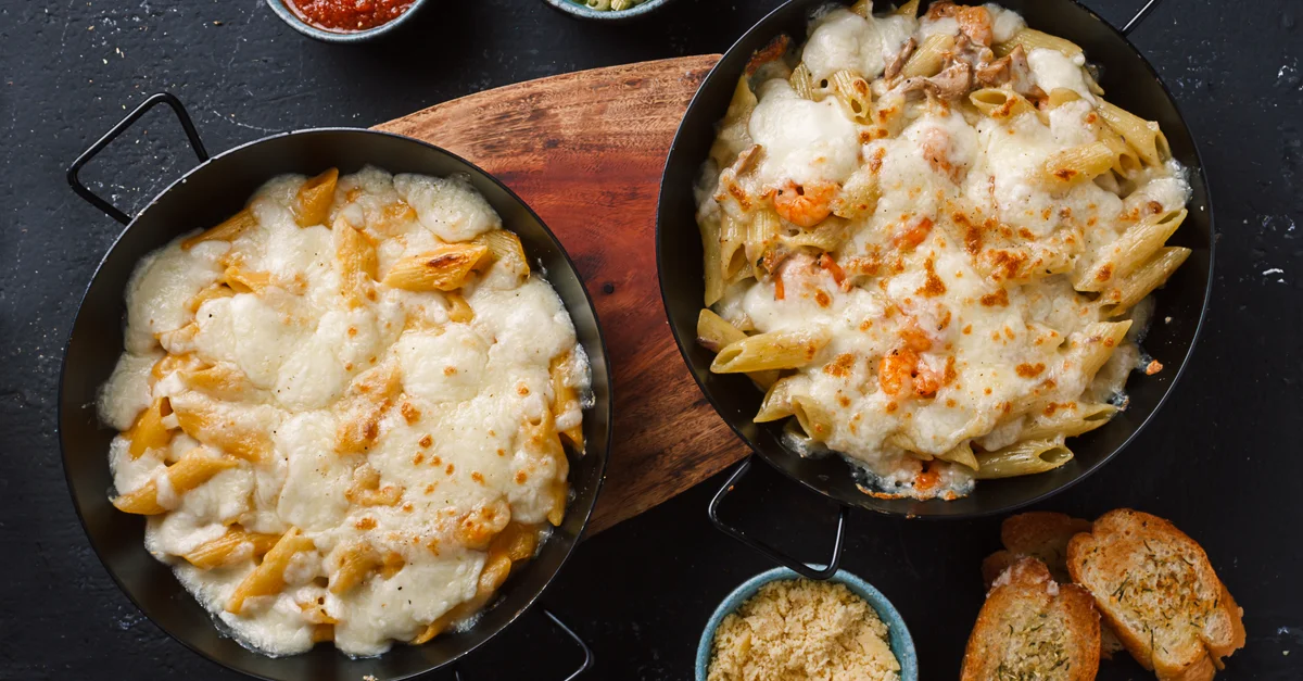 Vista desde arriba de penne al horno con queso, servido con salsas y pan.