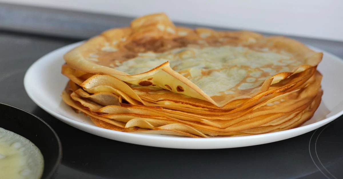 Una deliciosa pila de crepes doradas sobre un plato blanco, perfectas para el desayuno o el postre.