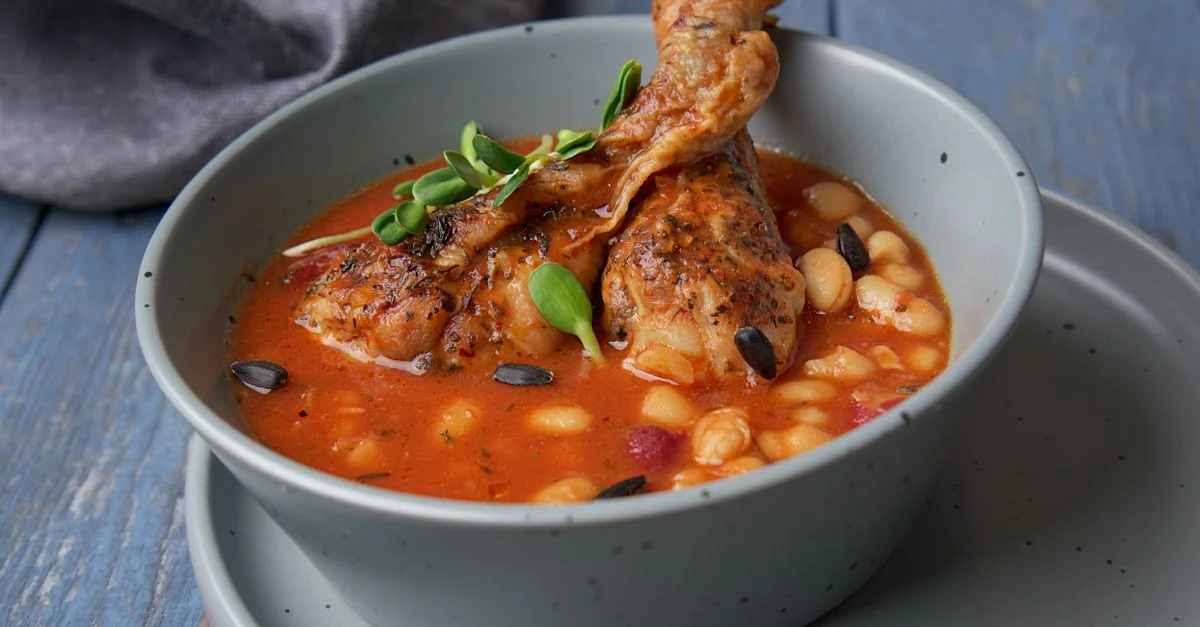 Disfrute del sabor de un abundante guiso de pollo y frijoles servido en un recipiente de cerámica azul.