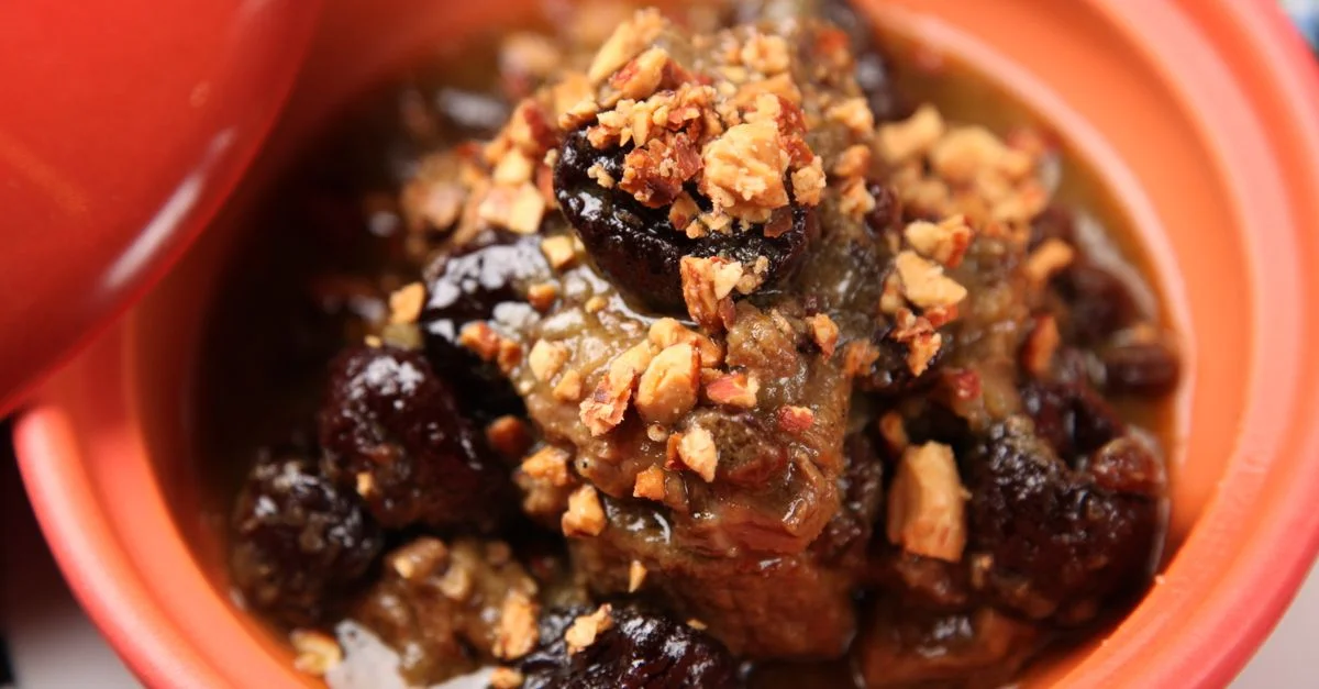 Acercamiento de un delicioso estofado de carne de res decorado con nueces, servido en un tazón de cerámica naranja.
