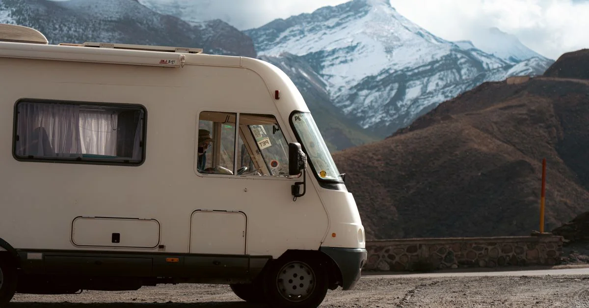 Autocaravana estacionada en una carretera con montañas nevadas al fondo, ofreciendo una escena de viaje aventurero.