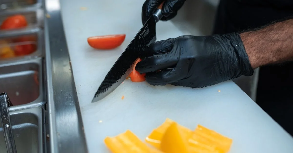 Chef con guantes corta pimientos en una cocina ocupada para la preparación de comidas.