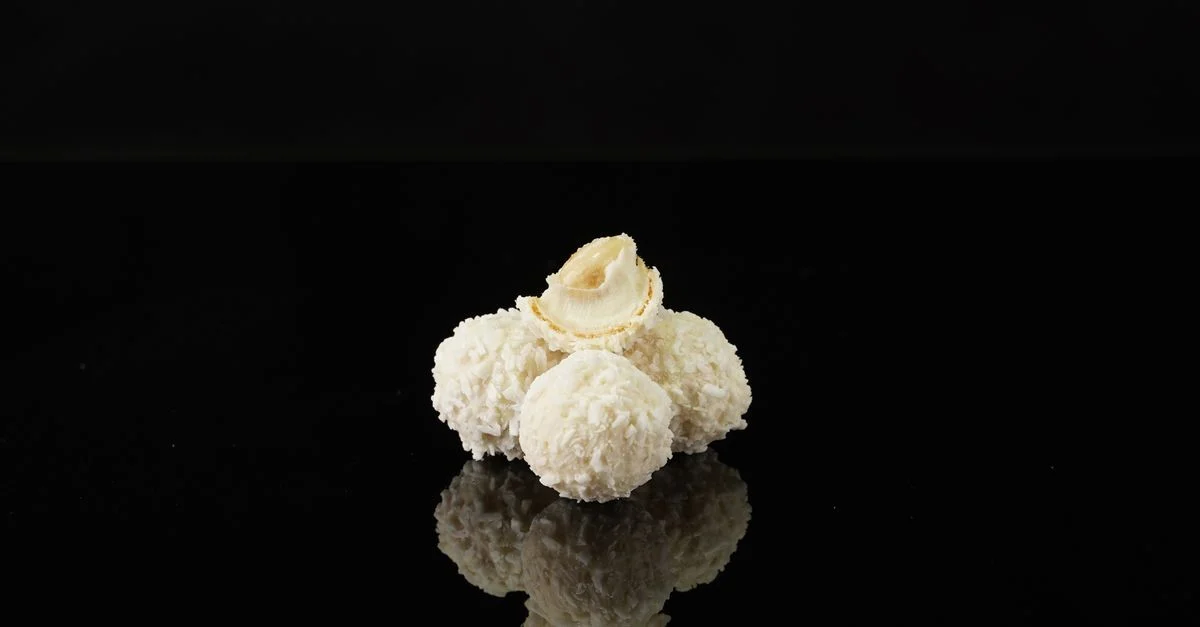 Foto minimalista de trufas de coco reflejando en una superficie negra brillante, perfecto para temas de postres.