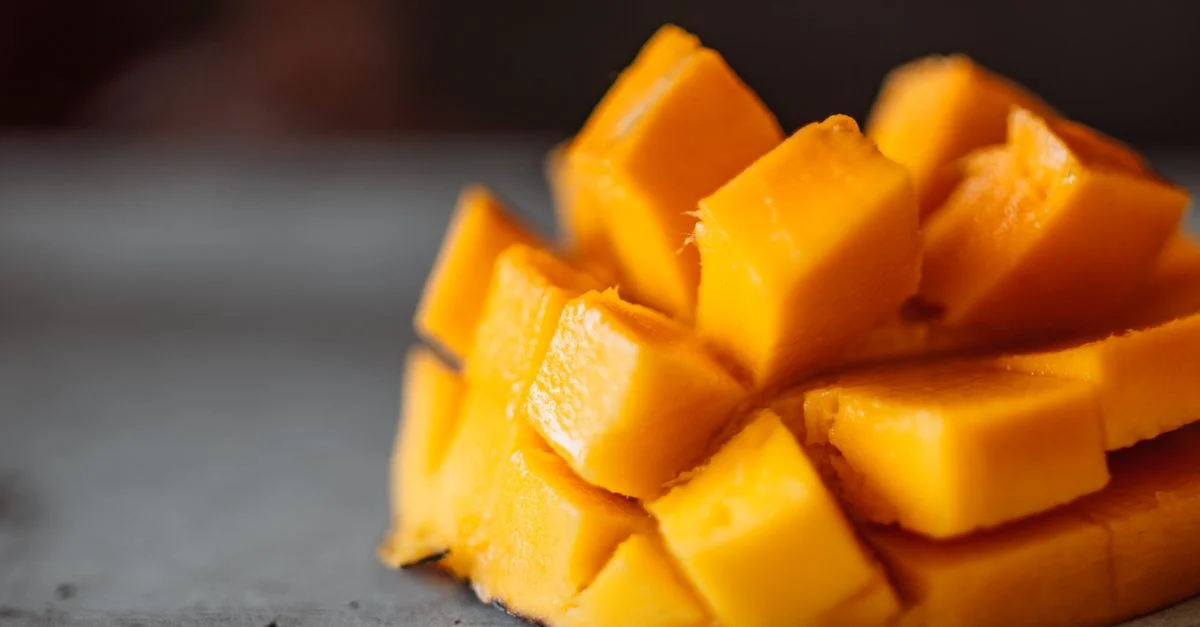 Primer plano de jugosos cubos de mango rebanados sobre una superficie gris, perfecto para refresco de verano.