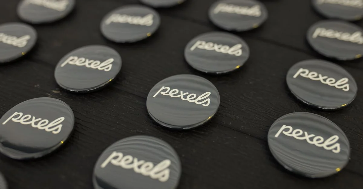 Vue rapprochée de plusieurs boutons de logo Pexels disposés soigneusement sur une surface sombre.