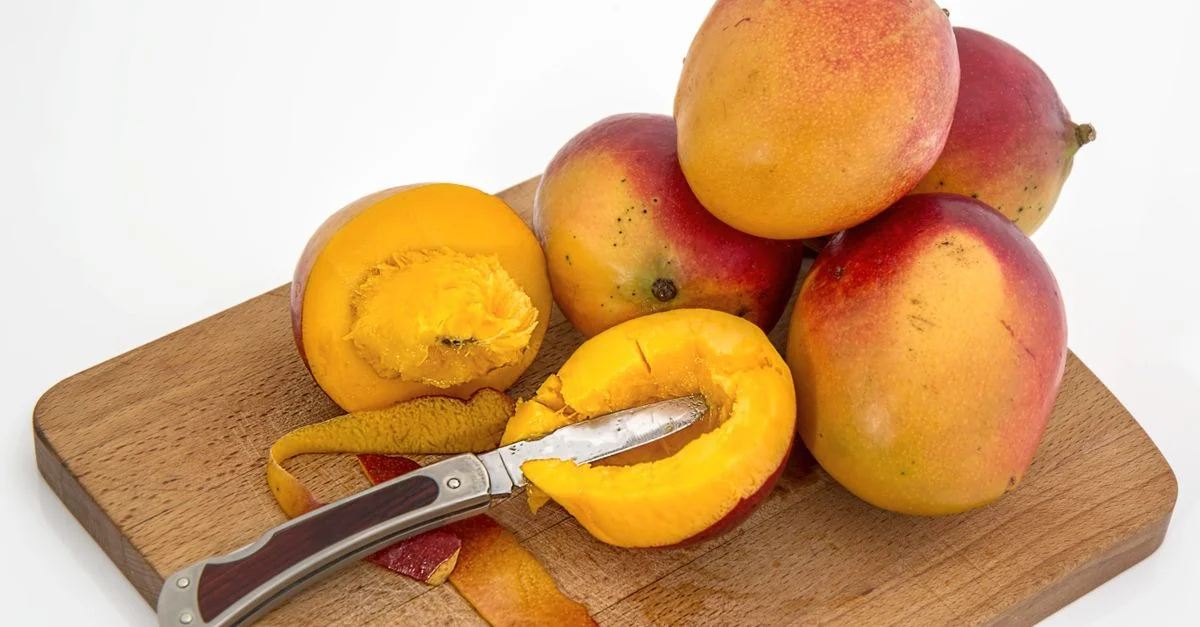 Mangos cortados y enteros sobre una tabla de madera con un cuchillo, mostrando la frescura vibrante de la fruta.