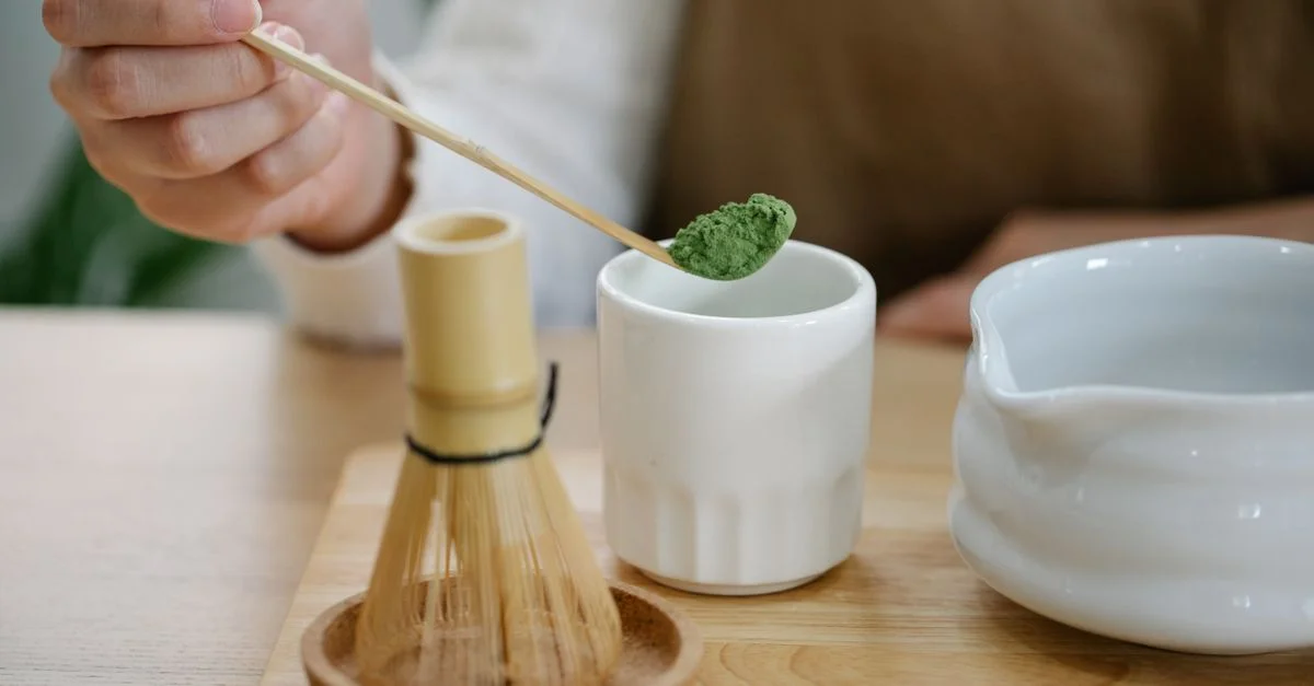 Una persona prepara té matcha utilizando herramientas tradicionales sobre una mesa de madera.
