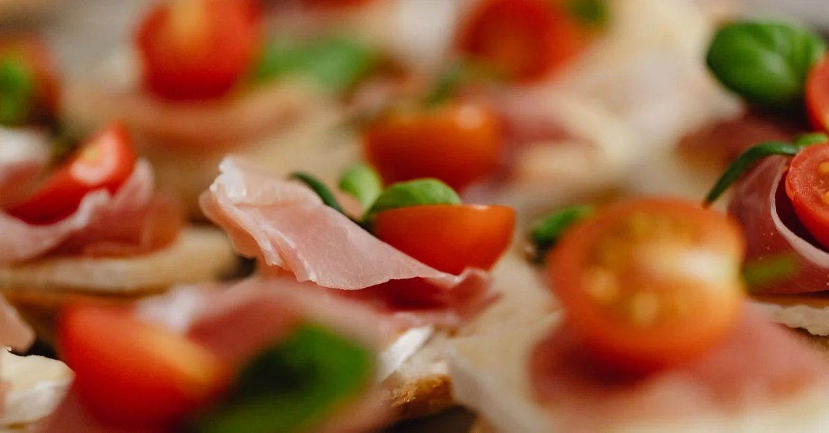 Canapés apetitosos cubiertos con jamón, tomates cherry y hojas de albahaca fresca.