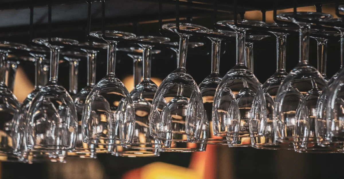Toma cercana de copas de vino boca abajo colgadas de un estante en un bar iluminado suavemente.