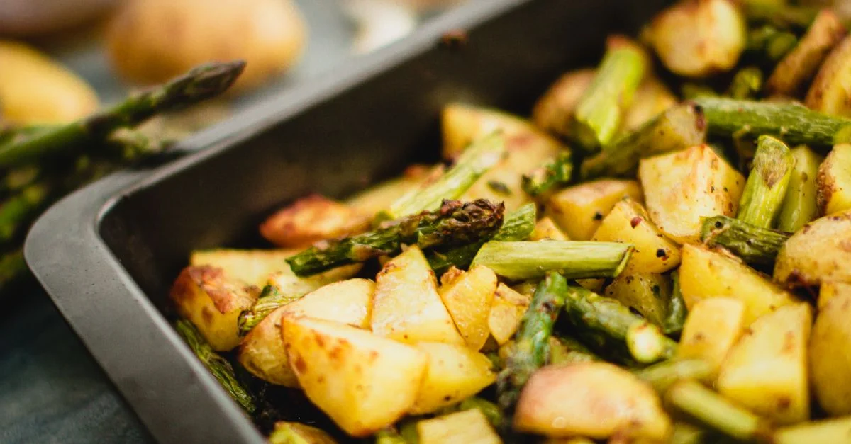 Toma en primer plano de espárragos y patatas asadas en una bandeja para hornear, perfecta para comidas veganas.